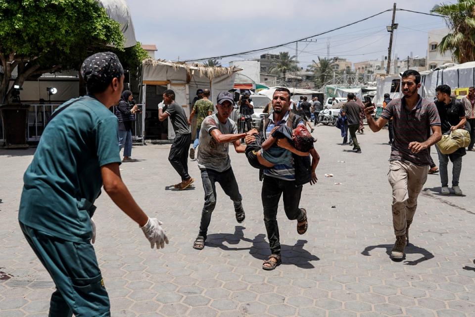 A man rushes a wounded child towards medics at Al-Aqsa Hospital (AFP via Getty Images)