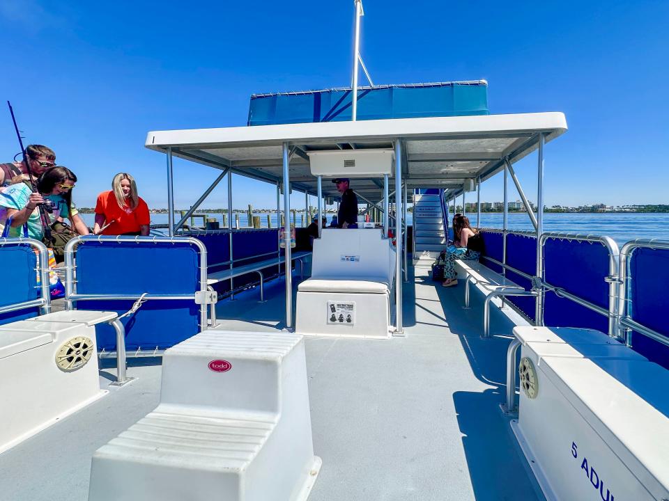 People on top deck of ferry, which has several white seats and blue railing, as it sails along blue water