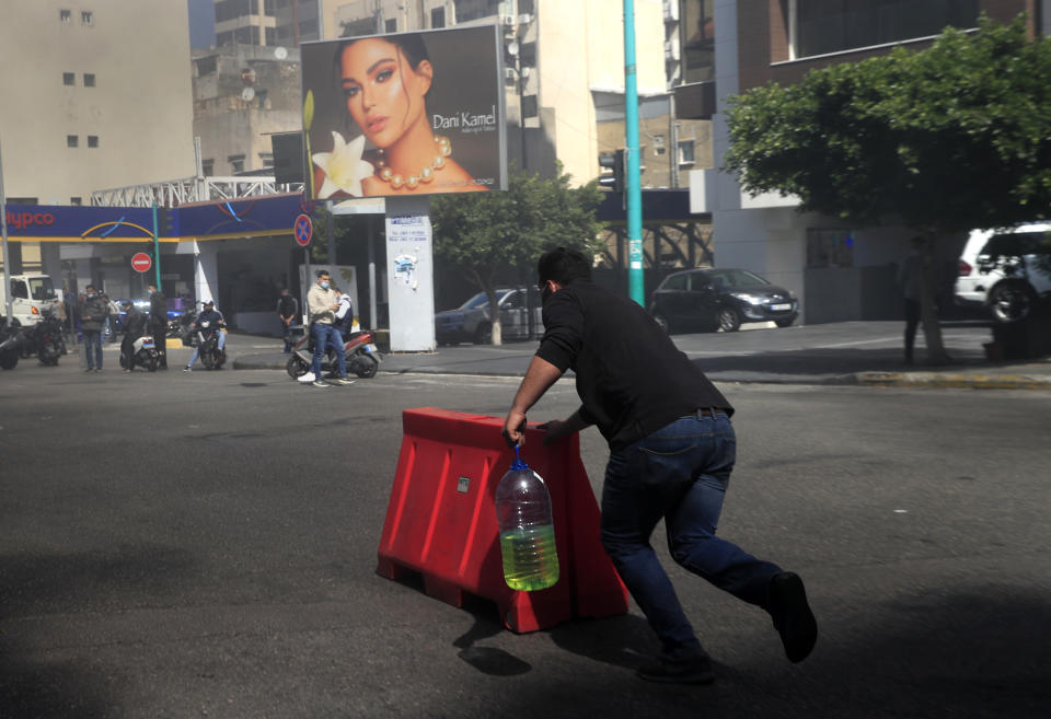 A protester pushes a plastic barrier and holds a container of gasoline to burn it to block a main road during a protest against the increase in prices of consumer goods and the crash of the local currency, in Beirut, Lebanon, Tuesday, March 16, 2021. Scattered protests broke out on Tuesday in different parts of the country after the Lebanese pound hit a new record low against the dollar on the black market. (AP Photo/Hussein Malla)