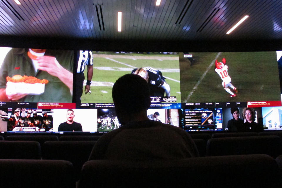 In this Nov. 20, 2018 photo, a customer watches video screens at a sportsbook in Atlantic City, N.J. On Thursday, March 11, 2021, BetMGM and Buffalo Wild Wings launched a program where special sports betting products are offered to customers at one of the chain's restaurants in New Jersey, Colorado, Indiana, Iowa, Tennessee and West Virginia. (AP Photo/Wayne Parry)