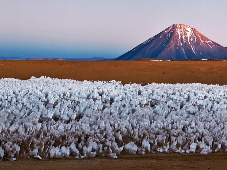 Structural white protrusions raise towards the sky in the foreground, while a picturesque volcano is seen in the background.