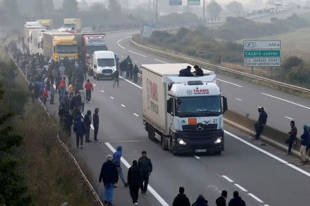 Migrants gather on the road as others board lorries that queue on the access road to reach the ferry terminal in Calais, France, October 3, 2015. REUTERS/Pascal Rossignol