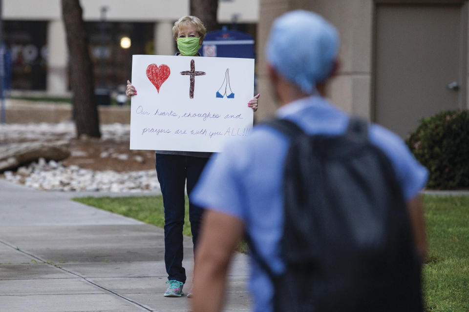 Beth Carrell holds up a sign that reads "Our hearts, thoughts and prayers are with you ALL!!!" as healthcare worker J.R. Gayton comes into work for a shift change at Medical Center Hospital Wednesday, Aug. 18, 2021, in Odessa, Texas. MCH is overwhelmed with COVID-19 patients with approximately 85 patients as of Tuesday. (Jacob Ford/Odessa American via AP)