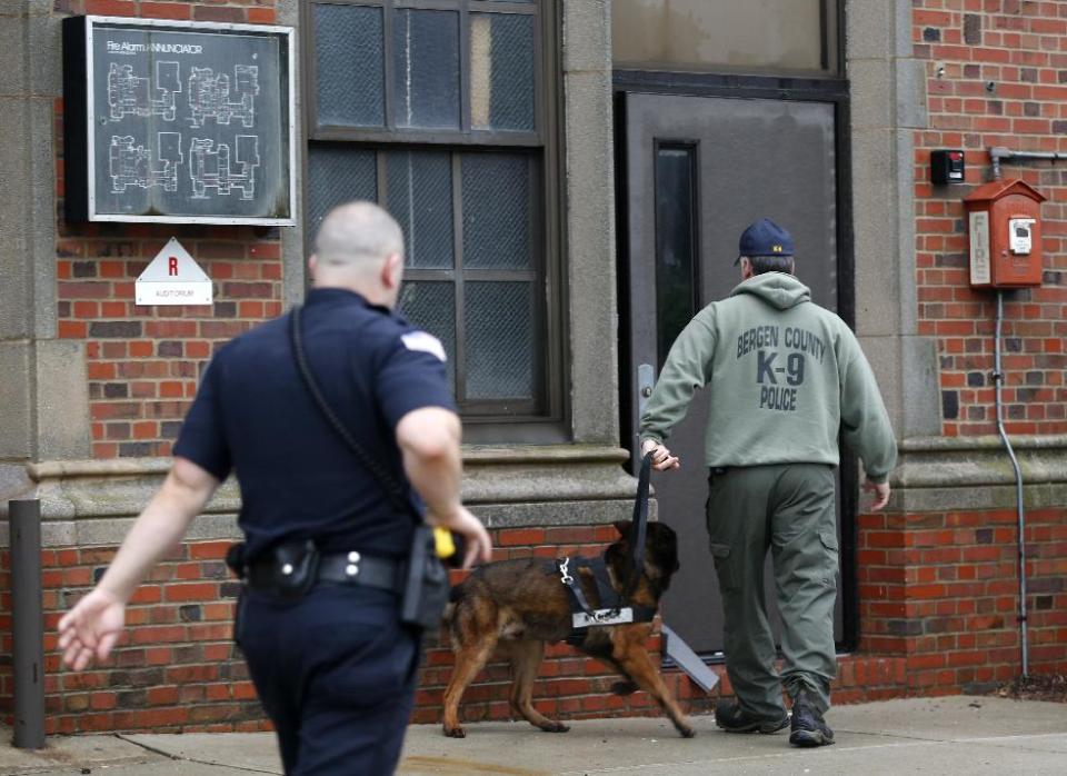 A Bergen County Police officer, right, walks with a police dog into Teaneck High School, where at least 60 students were arrested during an overnight break-in, Thursday, May 1, 2014, in Teaneck, N.J. Officers responded to a burglar alarm at the school around 2:30 a.m. Thursday, found urine in the hallways, petroleum jelly on doorknobs, desks flipped over and balloons throughout the building. (AP Photo/Julio Cortez)