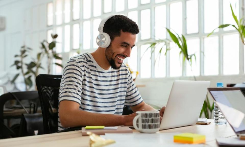 Laughing young man wearing headphones using laptop at desk in office