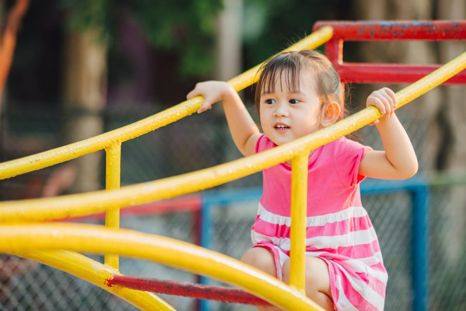 A girl in a pink dress on a yellow and red playground aparatus