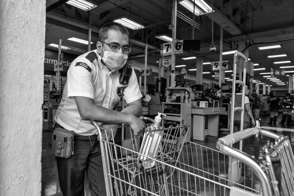 Un empleado de seguridad controla el acceso a un supermercado en el centro de Mérida durante la contingencia por COVID-19, permitiendo el acceso a una sola persona por familia y exigiendo la limpieza de manos con sanitizador antes de entrar.