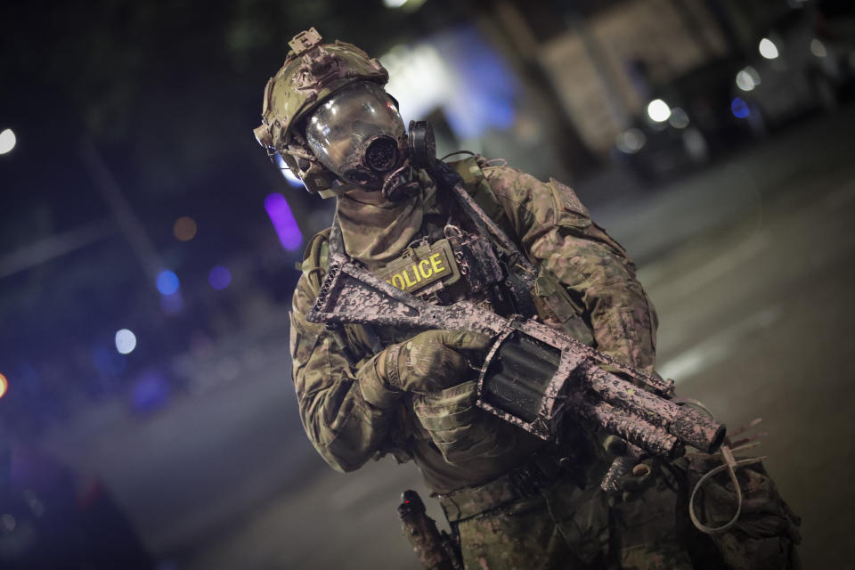 A federal officer holds a tear gas rifle during a Black Lives Matter protest at the Mark O. Hatfield U.S. Courthouse early Sunday, July 26, 2020, in Portland, Ore. On the streets of Portland, a strange armed conflict unfolds night after night. It is raw, frightening and painful on both sides of an iron fence separating the protesters on the outside and federal agents guarding a courthouse inside. This weekend, journalists for The Associated Press spent the weekend both outside, with the protesters, and inside the courthouse, with the federal agents, documenting the fight that has become an unlikely centerpiece of the protest movement gripping America. (AP Photo/Marcio Jose Sanchez)