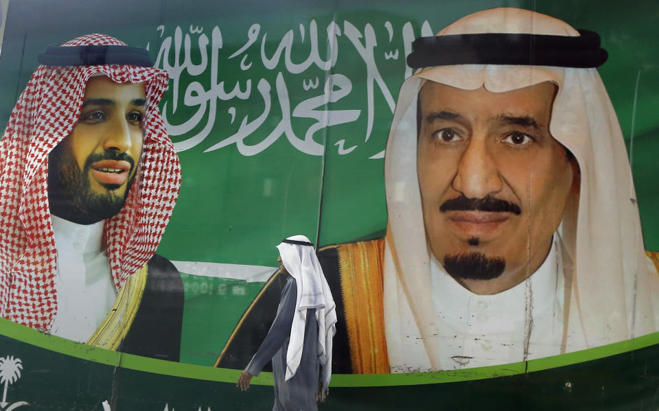 FILE - In this March 7, 2020 file photo, a man walks past a banner showing Saudi King Salman, right, and his Crown Prince Mohammed bin Salman, outside a mall in Jiddah, Saudi Arabia. Saudi Arabia announced Monday, May 11, 2020, it is tripling taxes on basic goods to 15% and will cut spending on major projects by around $26 billion as it grapples with blows from the coronavirus pandemic and low oil prices on its economy. (AP Photo/Amr Nabil, File)