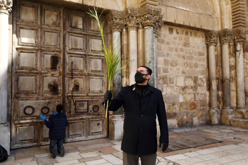 An Orthodox Christian worshipper wearing a mask holds a palm frond outside the closed doors of the Church of the Holy Sepulchre on Orthodox Palm Sunday amid the coronavirus disease (COVID-19) outbreak, in Jerusalem's Old City