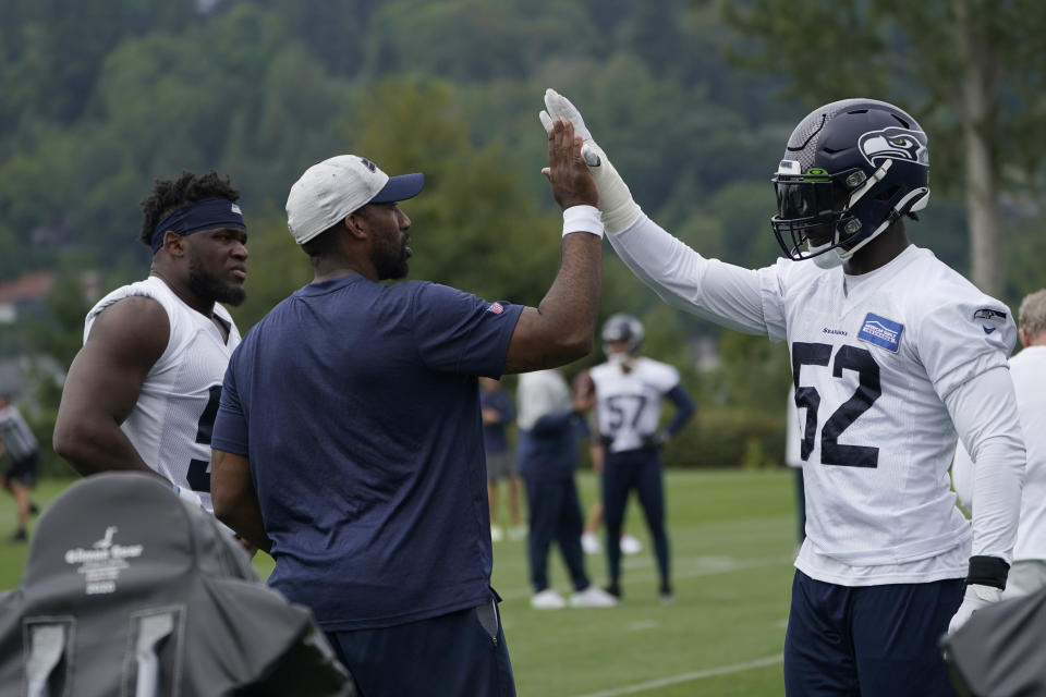 FILE - Aaron Curry, Seattle Seahawks defensive assistant and linebackers coach, center, high-fives defensive end Darrell Taylor during NFL football practice, Thursday, Aug. 19, 2021, in Renton, Wash. Now in his third season on the Seattle staff, Curry has seen his responsibilities grow along with his impact on those he’s coaching. (AP Photo/Ted S. Warren, File)