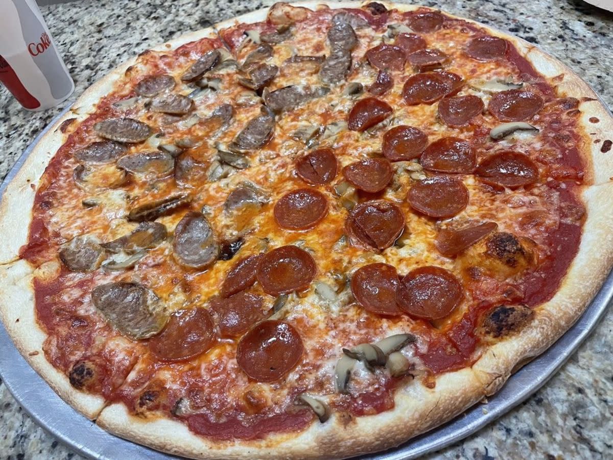 Half pepperoni and mushrooms and half sausage pizza, Amore Pizzeria, Queens, New York, on a table with a drink on the top left