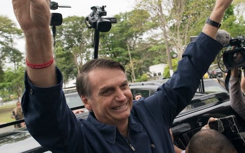 Presidential frontrunner Jair Bolsonaro, of the Social Liberal Party, flashes victory hand signs to supporters after voting at a polling station in Rio de Janeiro - Credit: AP