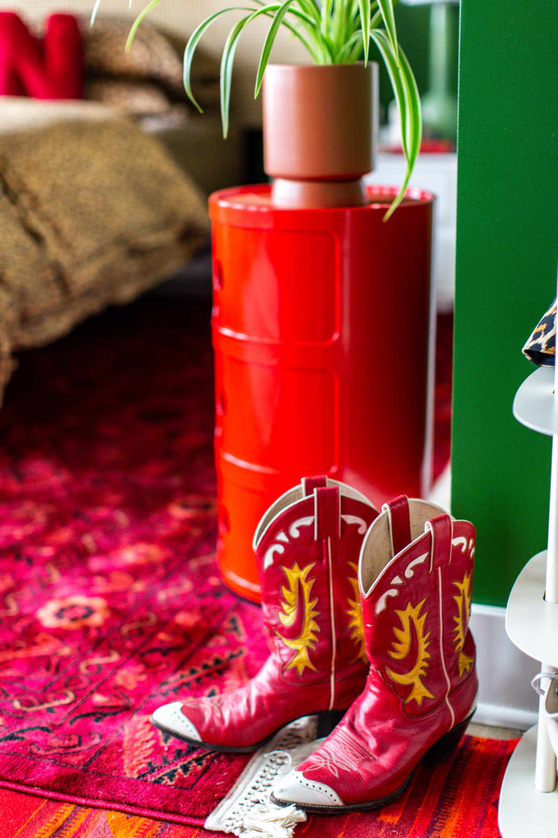 Red cowboy boots on red patterned rug. Green wall and red side table with spider plant