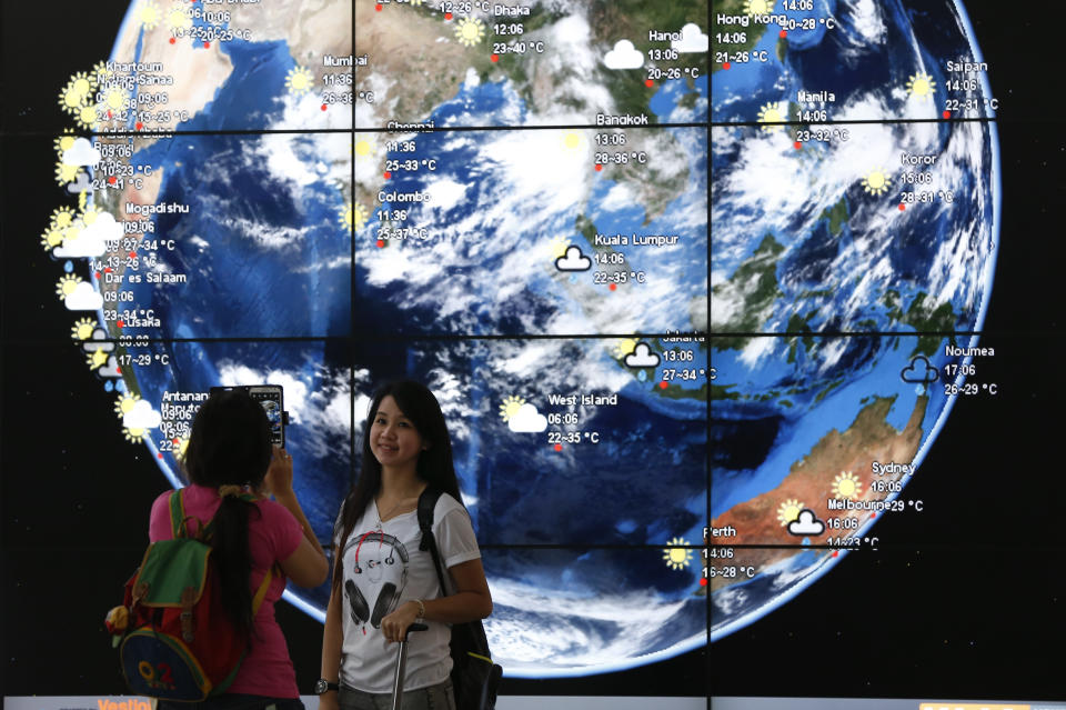 A Chinese girl is taken a picture in front of an electronic display showing the weather information of the cities in Asia at the Kuala Lumpur International Airport, in Sepang, Malaysia, Monday, March 17, 2014. When someone at the controls calmly said the last words heard from the missing Malaysian jetliner, one of the Boeing 777's communications systems had already been disabled, adding to suspicions that one or both of the pilots were involved in the disappearance of the flight. (AP Photo/Vincent Thian)