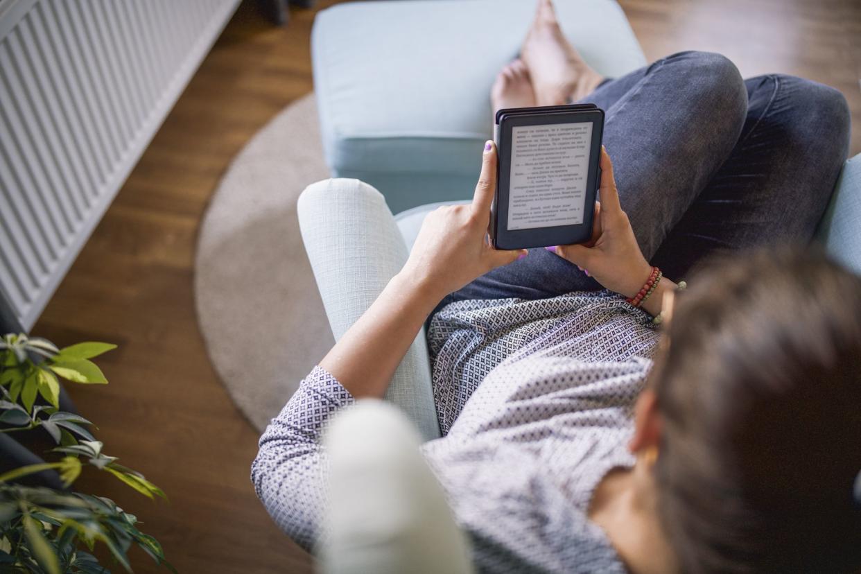 Unrecognizable woman is relaxing at her home with an E-book in her hands
