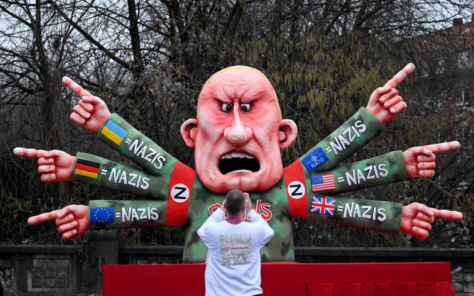 A man takes pictures of a carnival float featuring Vladimir Putin, who has six arms with the flags of Ukraine, Germany, Europe, Nato, the US and Britain, equating them all with nazis, during a Rose Monday street carnival parade in Dusseldorf - INA FASSBENDER/AFP