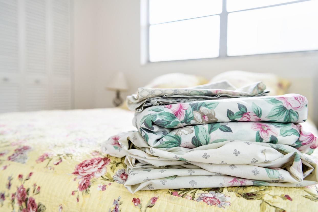 stack of bedroom linen with floral, flower pattern on top of bed with quilt