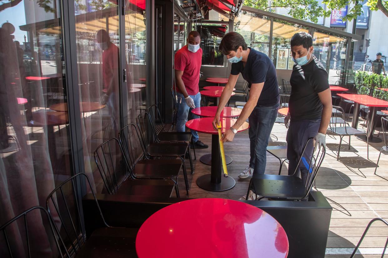 Pierre-Antoine Boureau, center, measures the space between tables as he prepares the terrace of a restaurant in order to respect social distancing in Paris on June 1, 2020. France is reopened its restaurants, bars and cafes on Tuesday as the country eased most restrictions amid the coronavirus crisis.