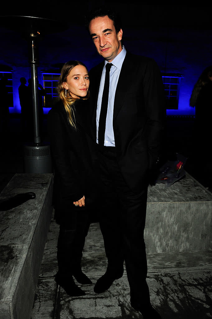 The two standing together, Mary-Kate in a black outfit and boots, and Olivier in a suit with a tie