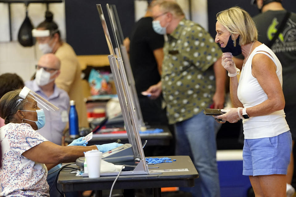 A voter, right, pulls down her mask for a Harris County election clerk before voting, Tuesday, July 14, 2020, in Houston. (AP Photo/David J. Phillip)