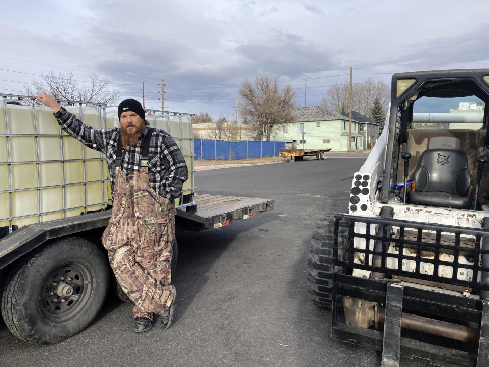 Micheal Weir, a contractor for cryptocurrency mining equipment company Elite Mining, stands next to a container of BitCool electronics coolant outside the company's facility in Cheyenne, Wyo. on Monday, Nov. 28, 2022. Wyoming has sought with several new laws to attract crypto-related businesses to the state and plans to keep doing so despite the industry's recent troubles. (AP Photo/Mead Gruver)