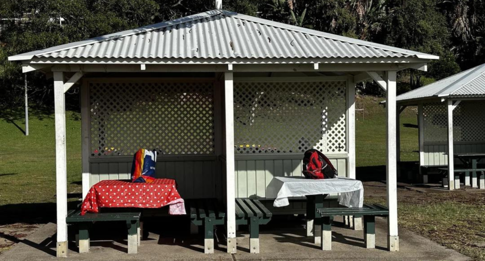 Picnic tables with Bronte beach with tablecloths and backpacks on them.