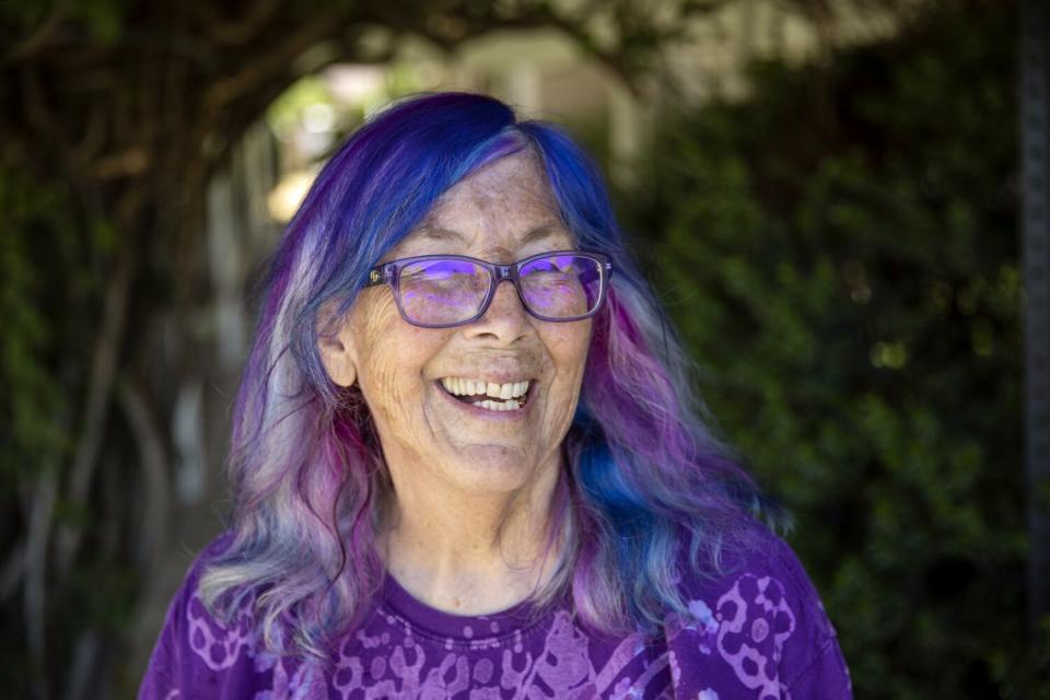 Leigh Adams, a laughing woman with purple-streaked silver hair, purple glasses and a purple T-shirt.