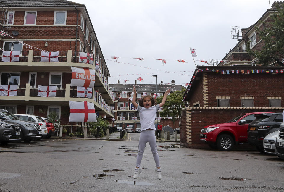 Marianne Hicks-Brisson jumps in the air as she poses for a photograph in the Kirby Estate adorned with English Cross of St. George flags in support of the England soccer team competing at the Euro 2020 soccer championships in Bermondsey, south London on June 29, 2021. (AP Photo/Tony Hicks)