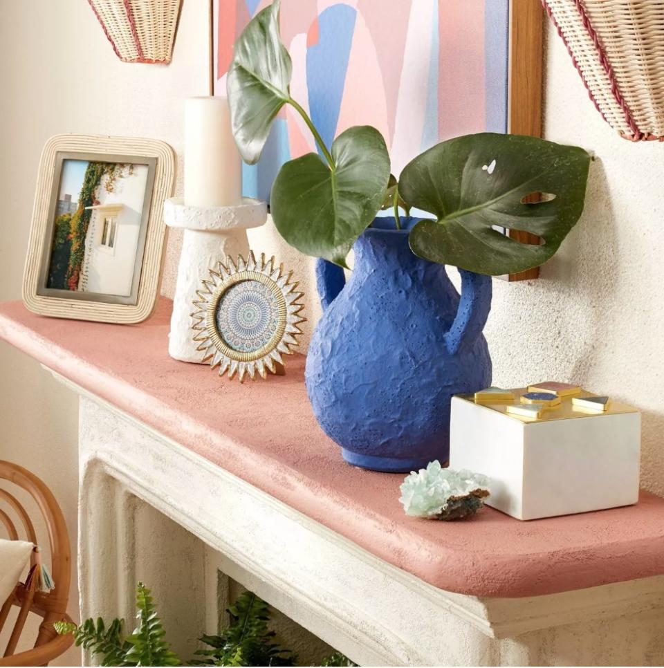 Round sun-shaped gold picture frame on pink mantle next to blue vase