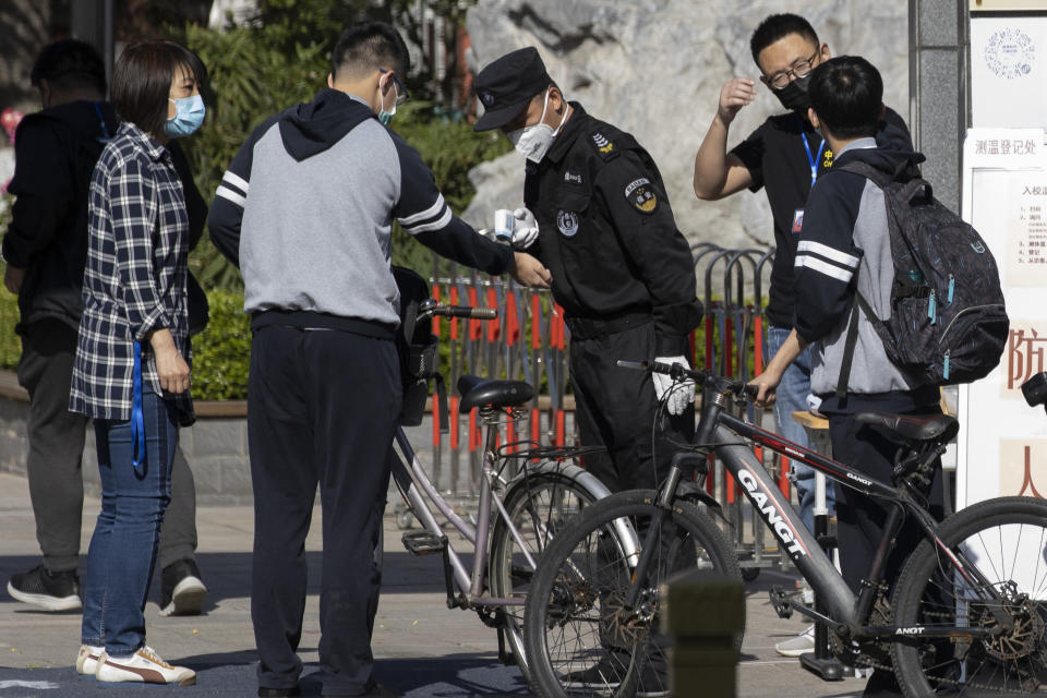 A security guard takes the temperature of a student arriving for the reopening of school at a middle school in Beijing on Monday, May 11, 2020. The Chinese capital partially reopen schools for some students on Monday as authorities push to restore normalcy after the lockdown to fight the coronavirus. (AP Photo/Ng Han Guan)