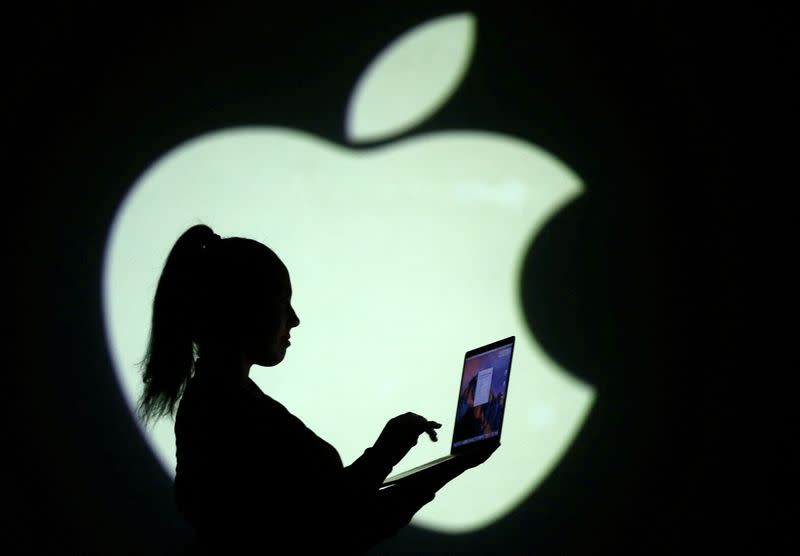 FILE PHOTO: Silhouette of laptop user is seen next to a screen projection of Apple logo in this picture illustration