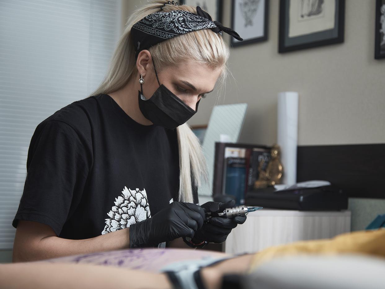Tattoo artist preparing gun in black shirt, mask, and bandana