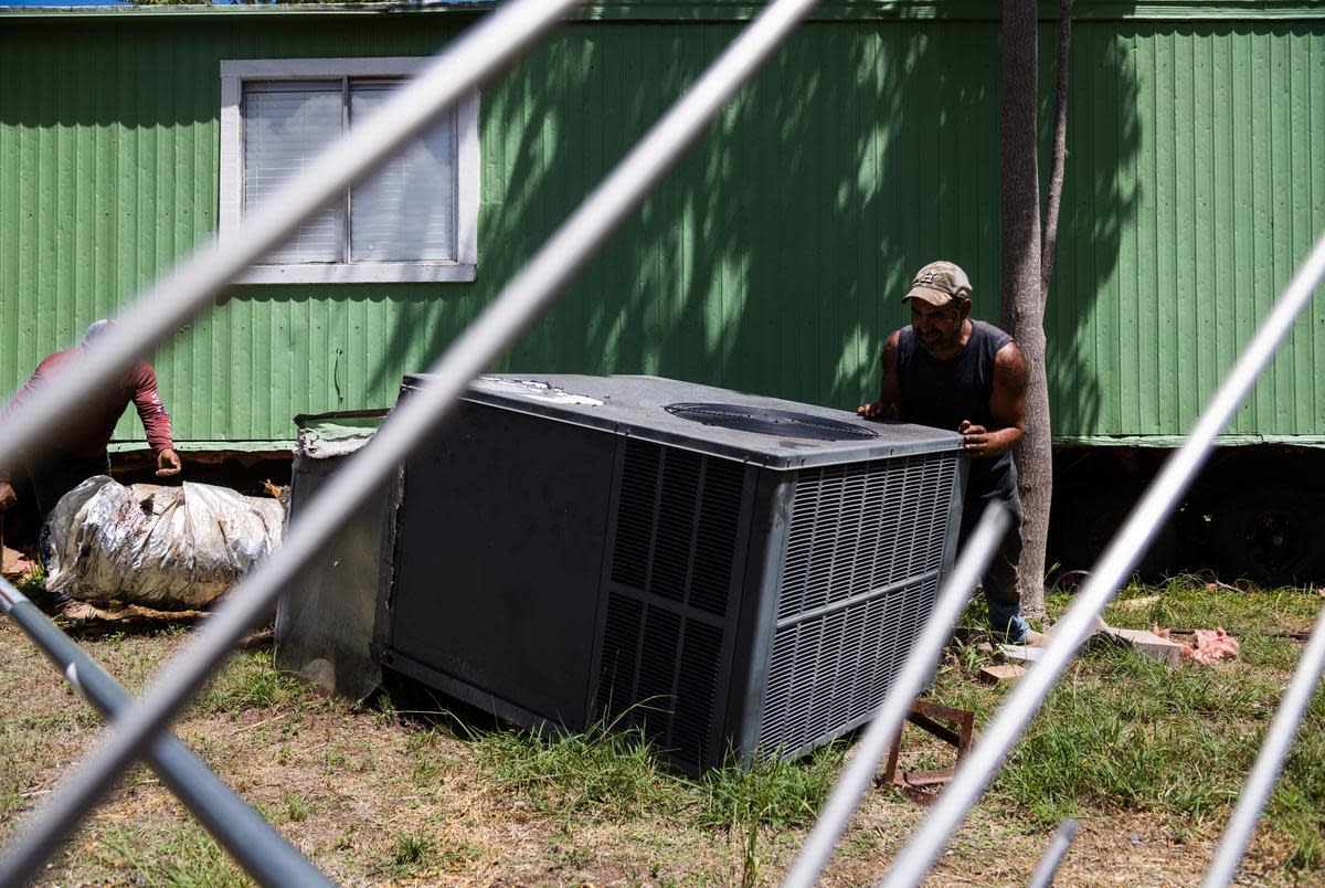 Workers remove an AC unit from Paola Valdez-Lopez's mobile home in order to tow it out of Congress Mobile Home Park in Austin on Aug. 29, 2022.