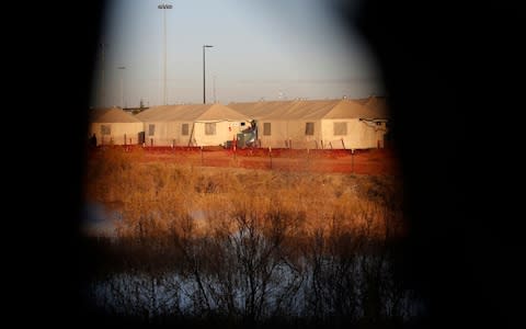 Tents show through a hole in the tarp that covers the fence of the Tornillo detention camp for migrant teenagers - Credit: AP