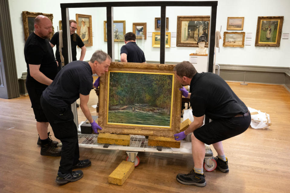 Three workers handling a framed painting for installation in an art gallery