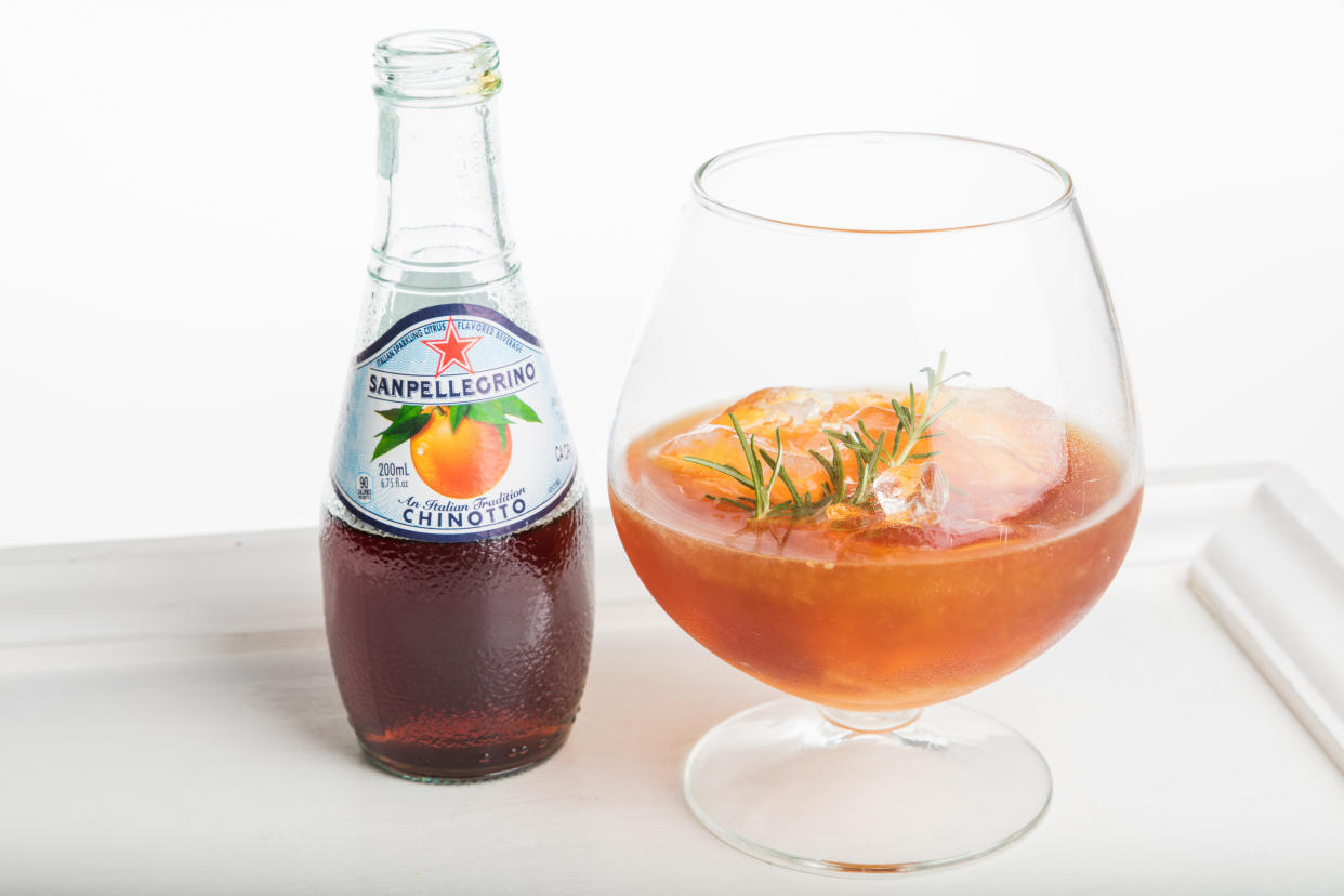 A glass containing a mocktail drink next to a bottle of San Pellegrino.
