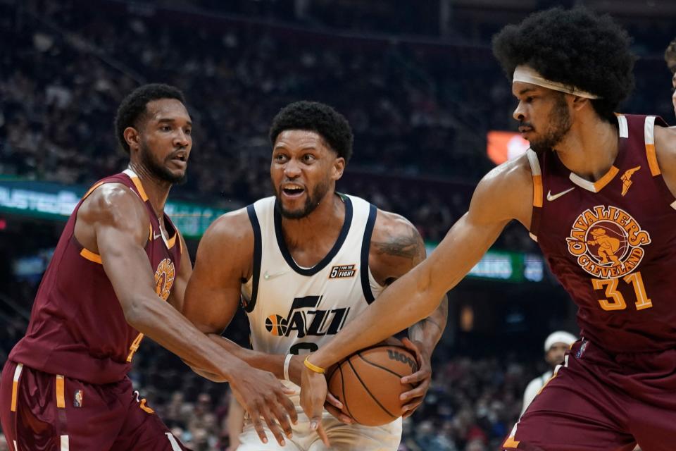 Utah Jazz's Rudy Gay, center, drives to the basket against Cleveland Cavaliers' Evan Mobley, left, and Cleveland Cavaliers' Jarrett Allen in the first half of an NBA basketball game, Sunday, Dec. 5, 2021, in Cleveland. (AP Photo/Tony Dejak)