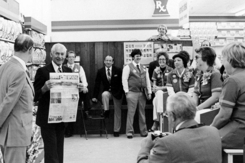 Sam Walton holding up a newspaper of a Walmart store's grand opening, while gathering with group of Walmart employees