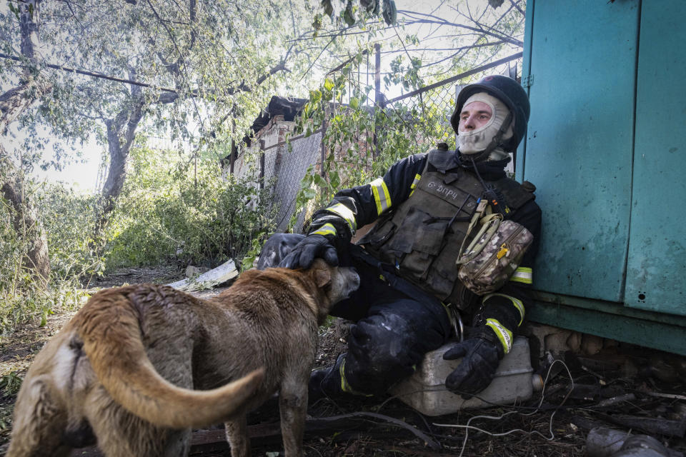 A firefighter pets a dog as he rests after putting out a fire in a private house hit by Russian shelling in Kharkiv, Ukraine, Friday, May 3, 2024. (AP Photo/Yevhen Titov)