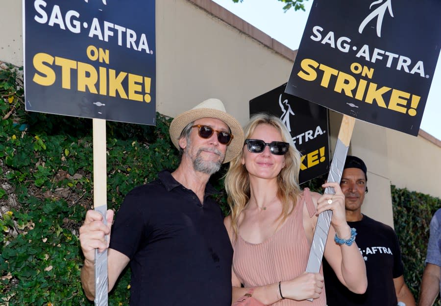 Actors Alan Ruck, left, and Justine Lupe, members of the cast of “Succession,” carry picket signs outside Warner Bros. studios on Tuesday, July 18, 2023, in Burbank, Calif. The actors strike comes more than two months after screenwriters began striking in their bid to get better pay and working conditions and have clear guidelines around the use of AI in film and television productions. (AP Photo/Chris Pizzello)