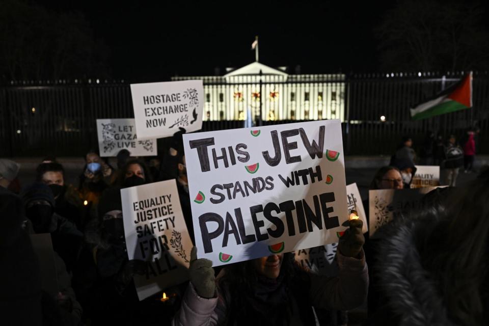 People hold up signs outside an illuminated white mansion. One says: "This Jew stands with Palestine."