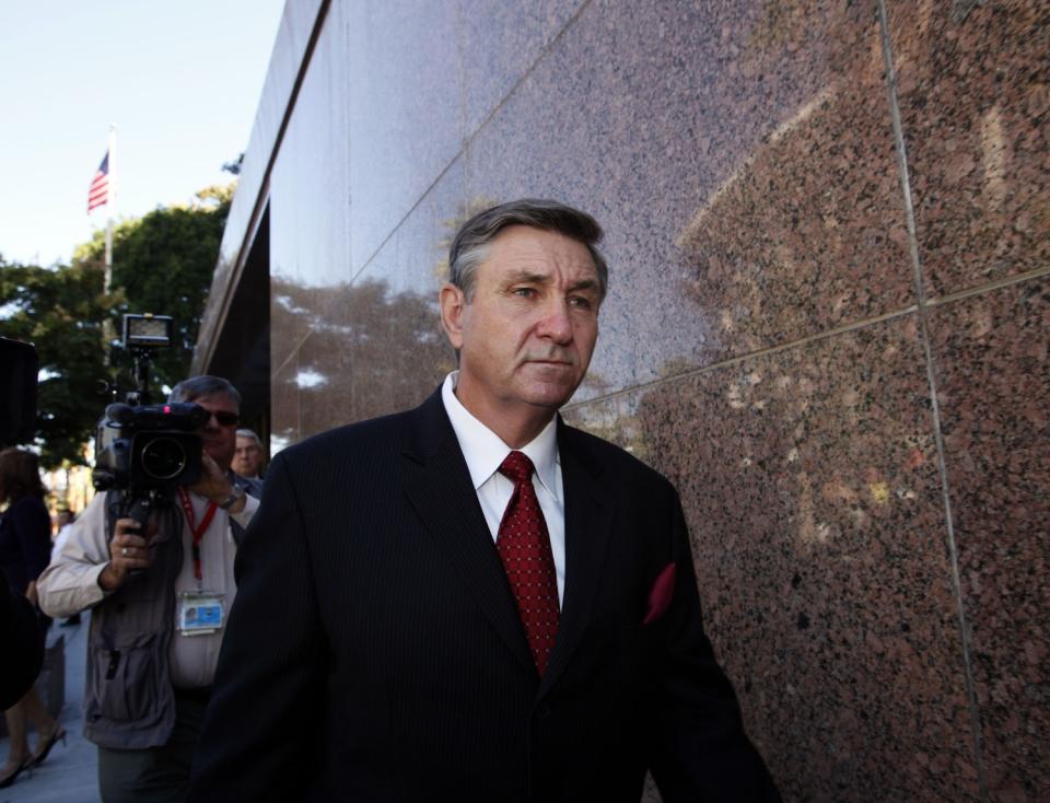 A white man in suit and tie is followed by a videographer