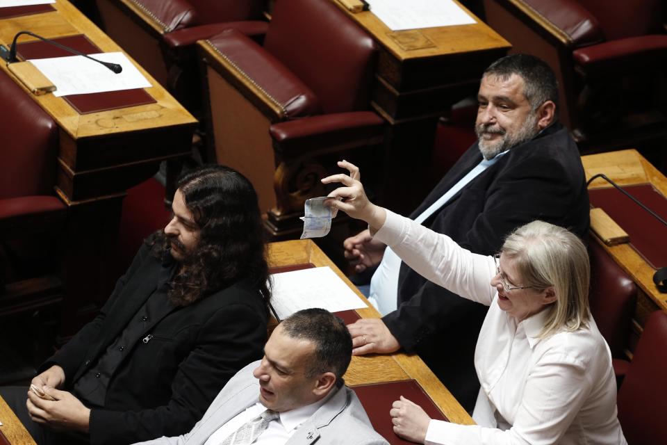 Golden Dawn lawmaker Eleni Zaroulia, surrounded by other deputies from the Nazi-inspired party, mockingly waves euro banknotes in the air as former party lawmaker Chryssovalandis Alexopoulos addresses Parliament in Athens, on Wednesday, May 7, 2014. Golden Dawn has labelled Alexopoulos a traitor and sellout for leaving the party while keeping his parliamentary seat. Parliament on Wednesday voted to lift Alexopoulos' immunity from prosecution so that he can face charges of allegedly running a criminal organization. All 16 of the party's lawmakers face the same charges, following a judicial crackdown on Golden Dawn last year after the murder of a left wing musician, allegedly by a party supporter. (AP Photo/Petros Giannakouris)