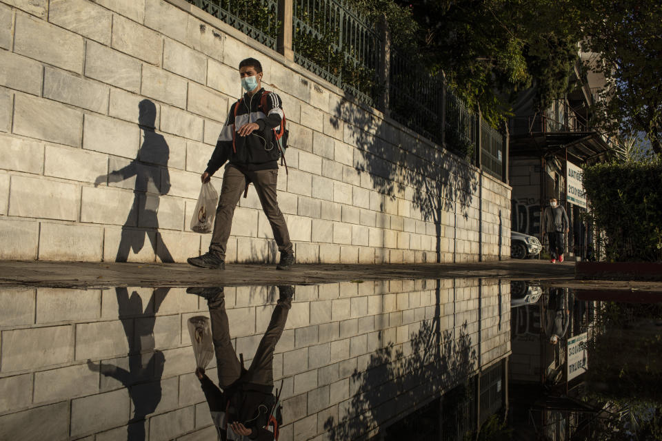 A man wearing a face mask to prevent the spread of COVID-19 is reflected in a puddle as he walks in central Athens, Thursday, Oct. 29, 2020. Greece is seeing a record-breaking jump in the number of confirmed coronavirus cases for the second consecutive day, with 1,547 new cases announced Wednesday, Oct 28, and 10 new deaths. (AP Photo/Petros Giannakouris)