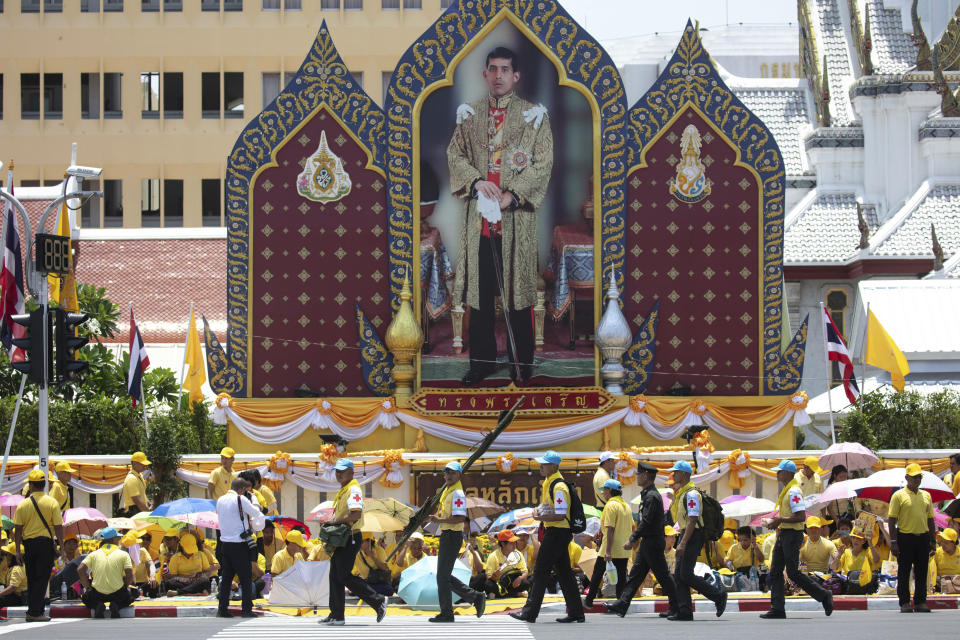 First aid workers walk pass a portrait of King Maha Vajiralongkorn during a series of his coronation ceremonies Sunday, May 5, 2019, in Bangkok, Thailand. King Maha Vajiralongkorn was officially crowned amid the splendor of the country's Grand Palace, taking the central role in an elaborate centuries-old royal ceremony that was last held almost seven decades ago. (AP Photo/Wason Wanichakorn)