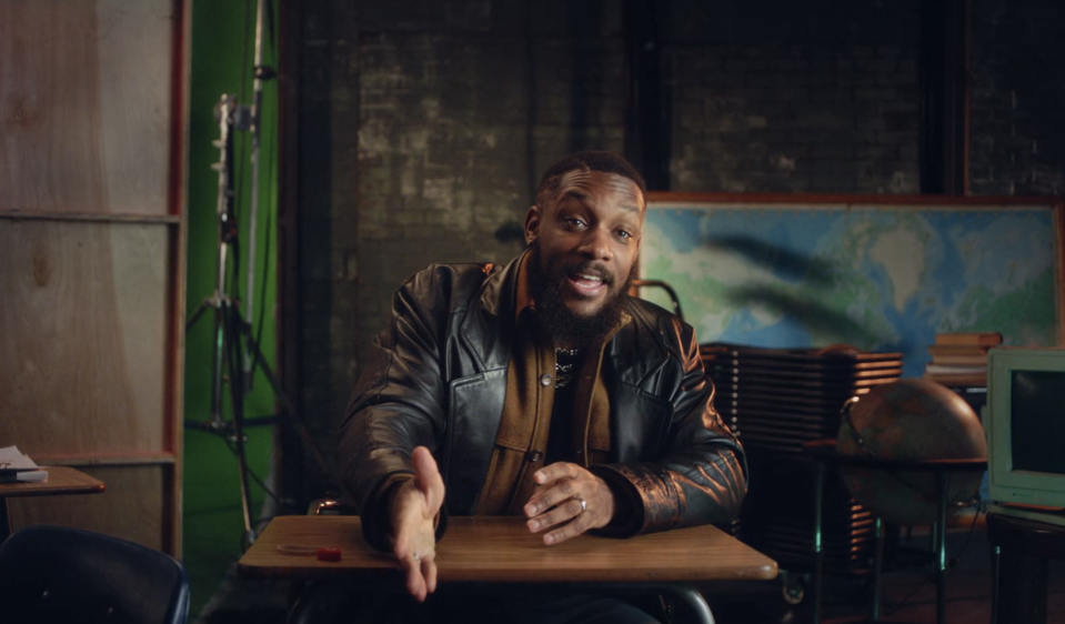 Bryan with a beard sitting at a desk, gesturing with his hands, wearing a leather jacket