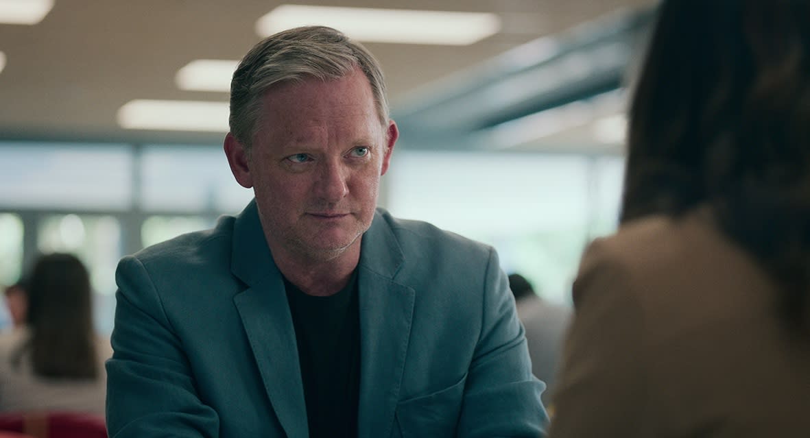  Daniel Lang (Douglas Henshall), wearing a suit, sits at a table looking at a woman sitting opposite him, who has her back to the camera 