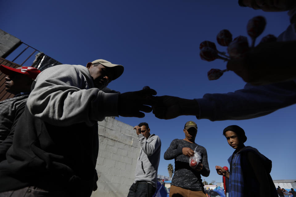 In this Dec. 3, 2018 photo, a customer buys a lollipop from Honduran migrant Victor Cardona, 32, right, who set up a stand selling candy and fried pork skin chips at the entrance to the former concert venue Barretal, now serving as a shelter for more than 2000 migrants, in Tijuana, Mexico. Facing the possibility of a months-long wait in Tijuana before even having an opportunity to request asylum in the United States, members of the migrant caravans that have arrived in Tijuana are looking for work. Some are creating their own informal businesses. (AP Photo/Rebecca Blackwell)