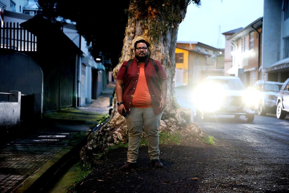 Man stands next to a tree by the side of the road.